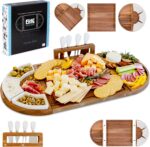 A large, brown acacia wood charcuterie board set with cheese knives and ceramic dishes, displaying a spread of snacks.