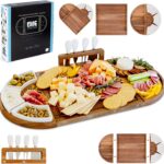 A large, brown acacia wood charcuterie board set with cheese knives and ceramic dishes, displaying a spread of snacks.