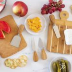 A four-piece Totally Bamboo cheese tool set with brown bamboo handles and silver stainless steel blades, arranged on a surfac